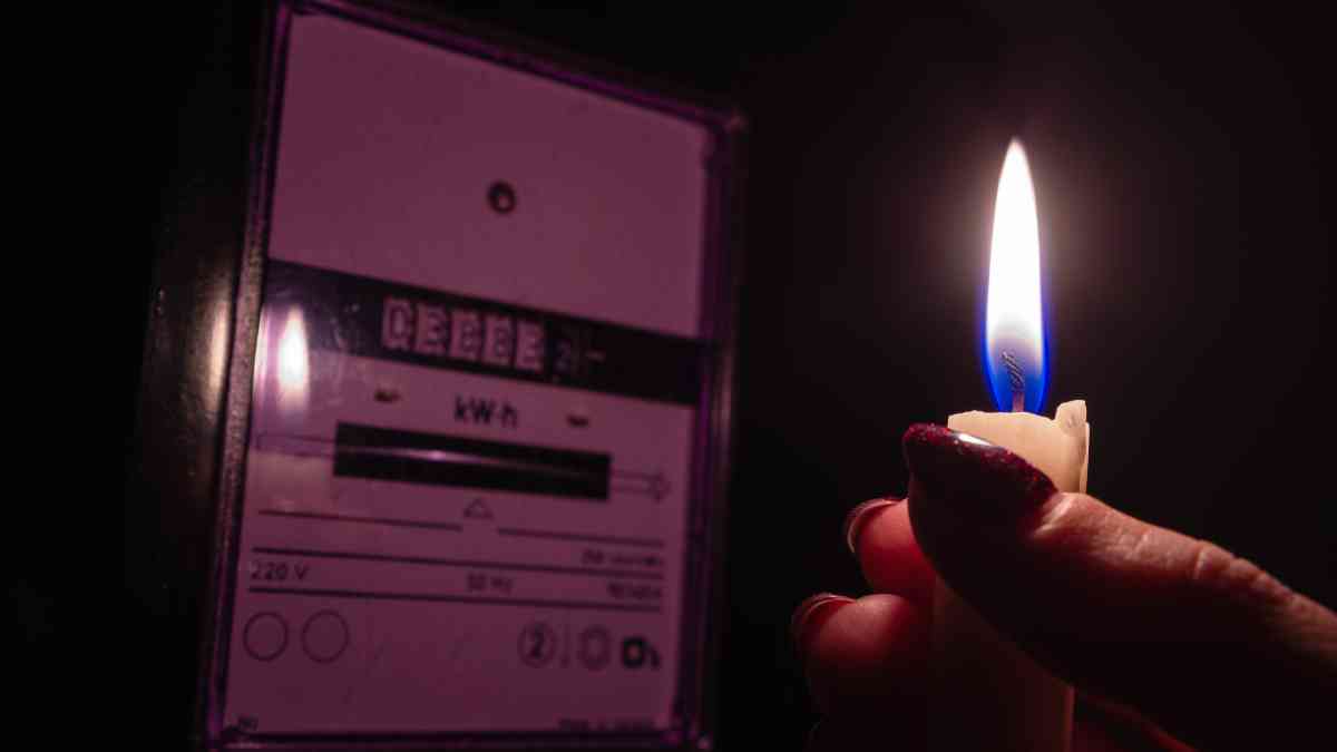 Candle shining light in the dark near electricity meter during power outage at home